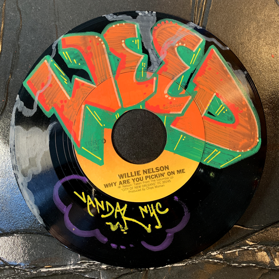 The word WEED hand lettered on 7" vinyl record. The record is Willie Nelson's Why Are You Pickin' On Me.